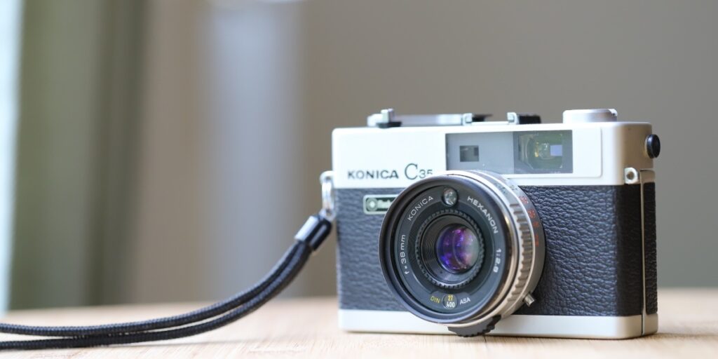 木製テーブルに置かれたヴィンテージのKonica C35フィルムカメラの実物写真。出張買取対象のクラシックカメラやコレクション品として紹介。